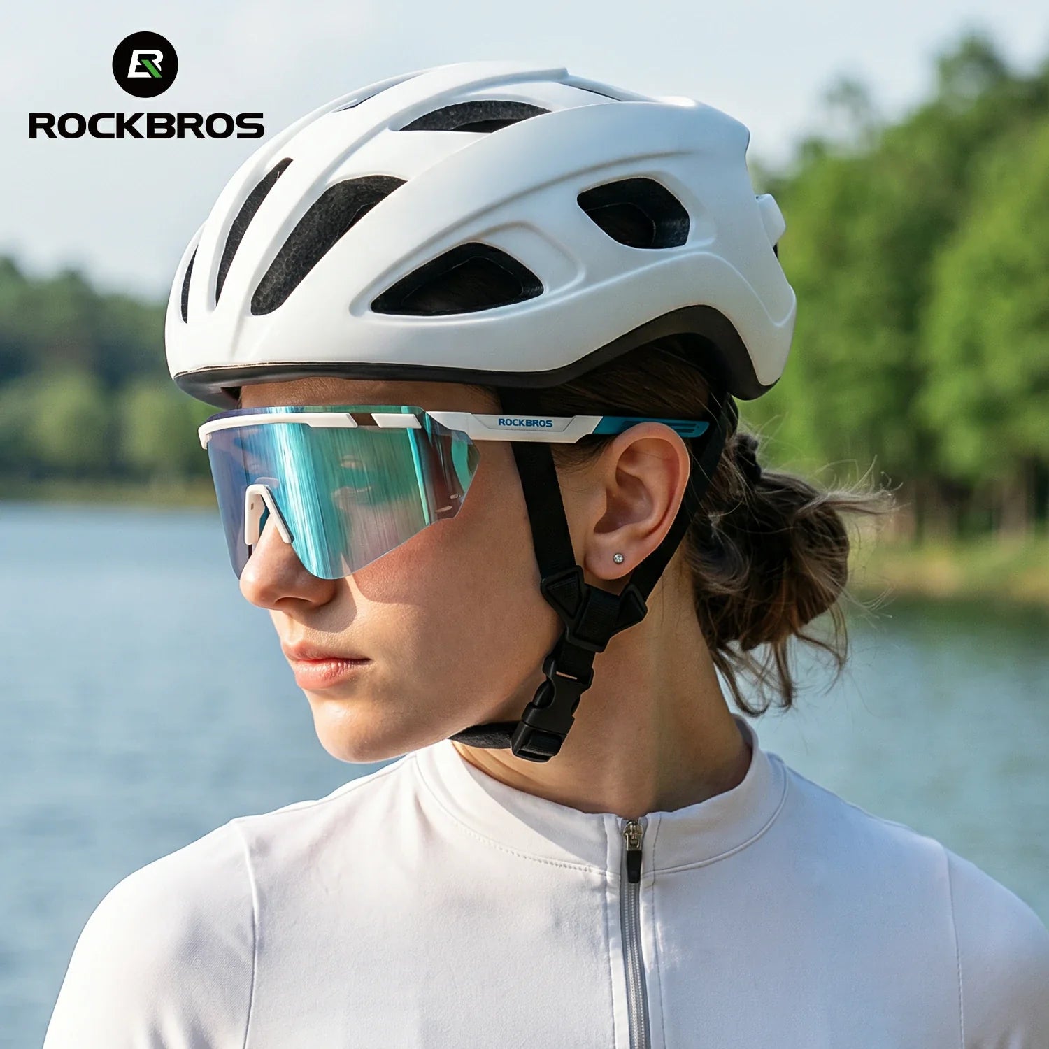 A woman in a white cycling jersey wearing a white Rockbros cycling helmet and mirrored shield glasses, photographed outdoors with water and trees in the background. #Color_Blue