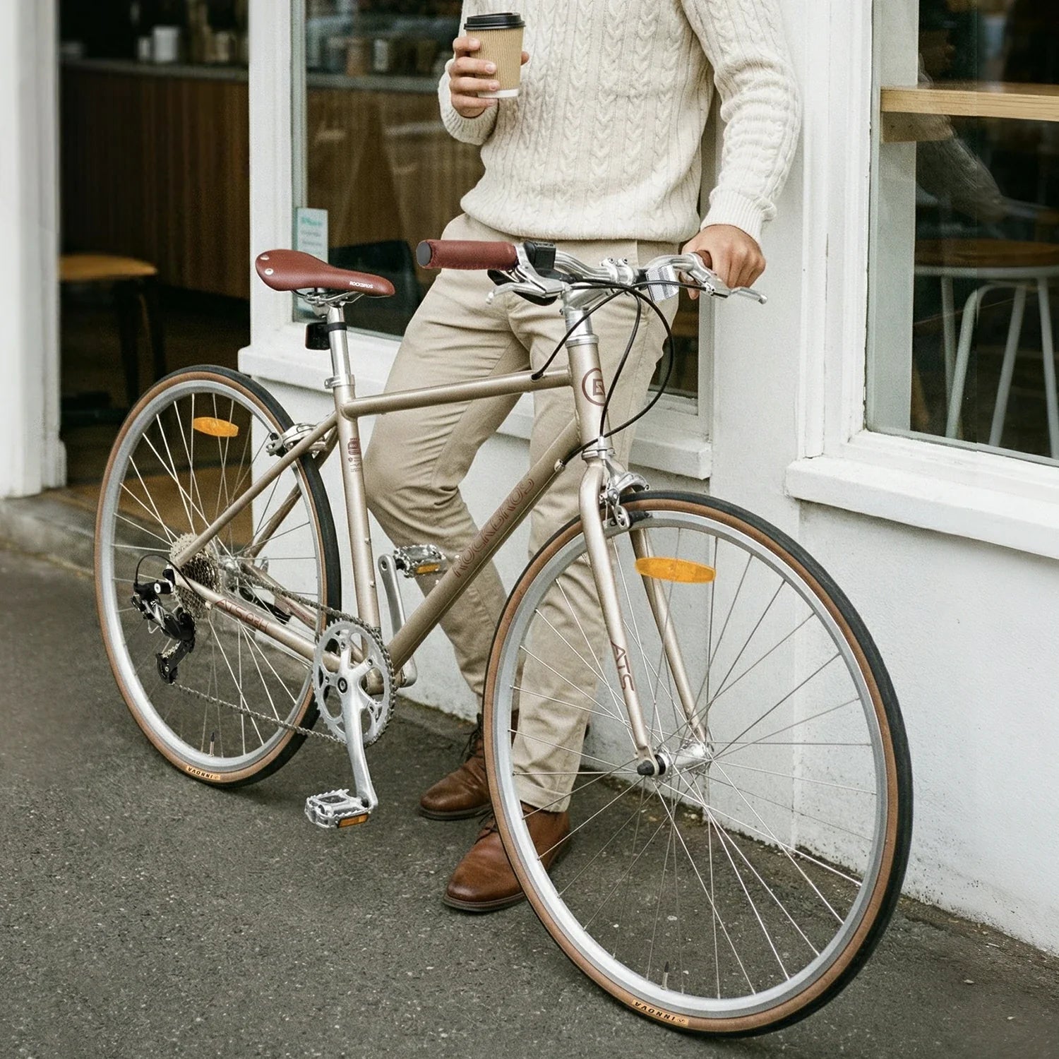 Person with a bicycle and a coffee cup standing outside a building.