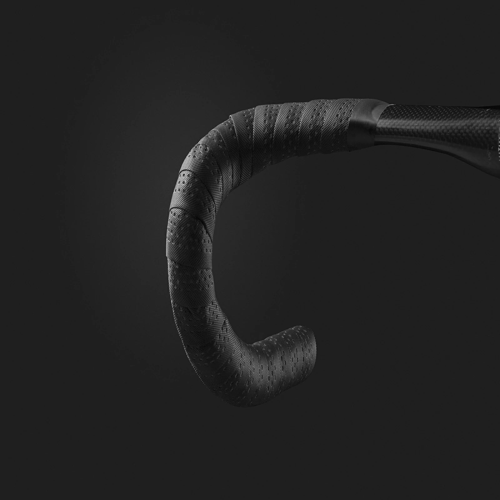 Close-up of a black drop handlebar with textured grip tape and a carbon fiber-look section, shown against a dark gray background. #Color_Black