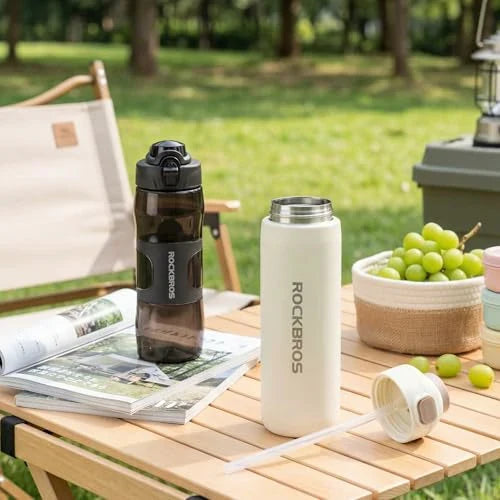 Two water bottles on a picnic table with greenery in the background