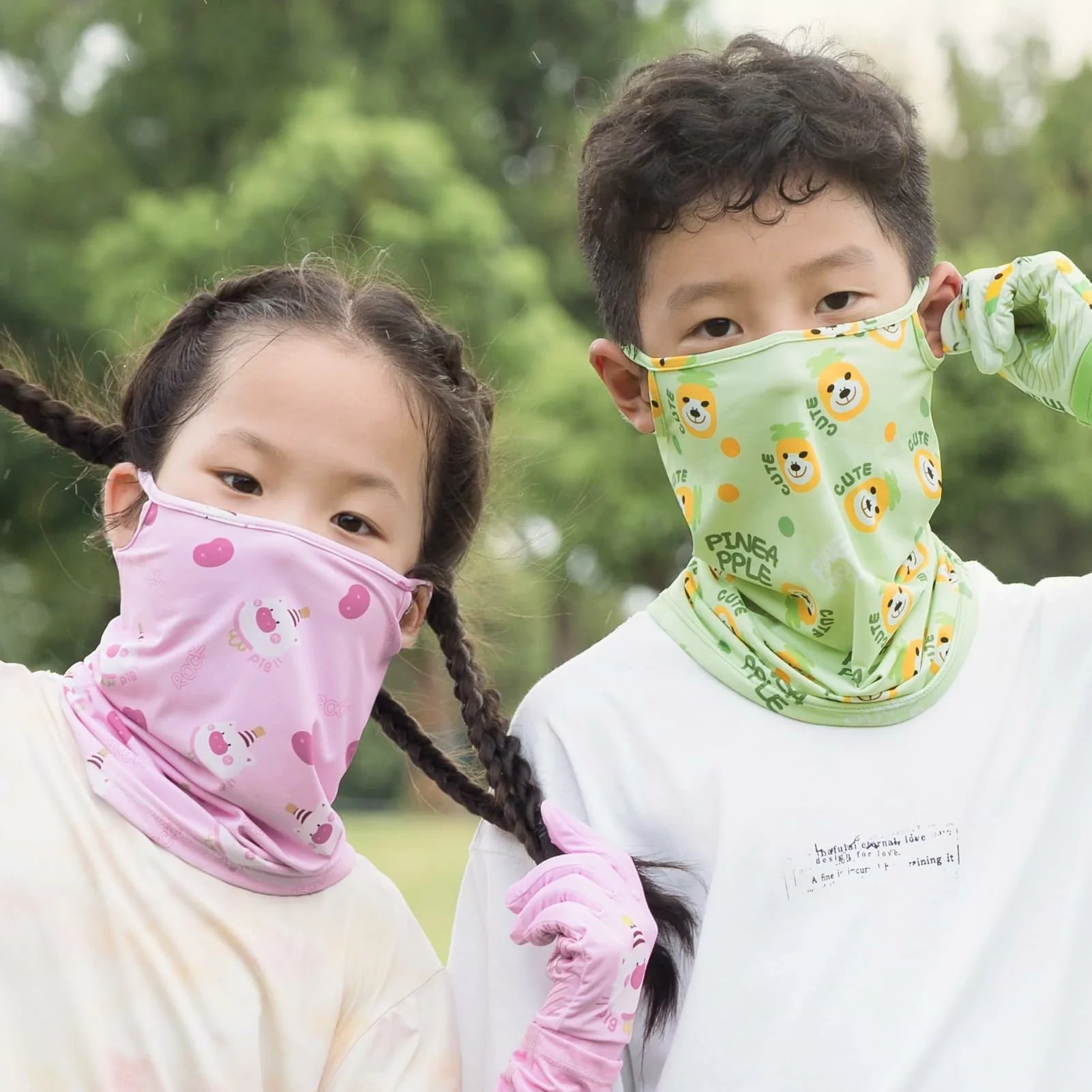 Two children wearing colorful neck gaiters outdoors with greenery in the background