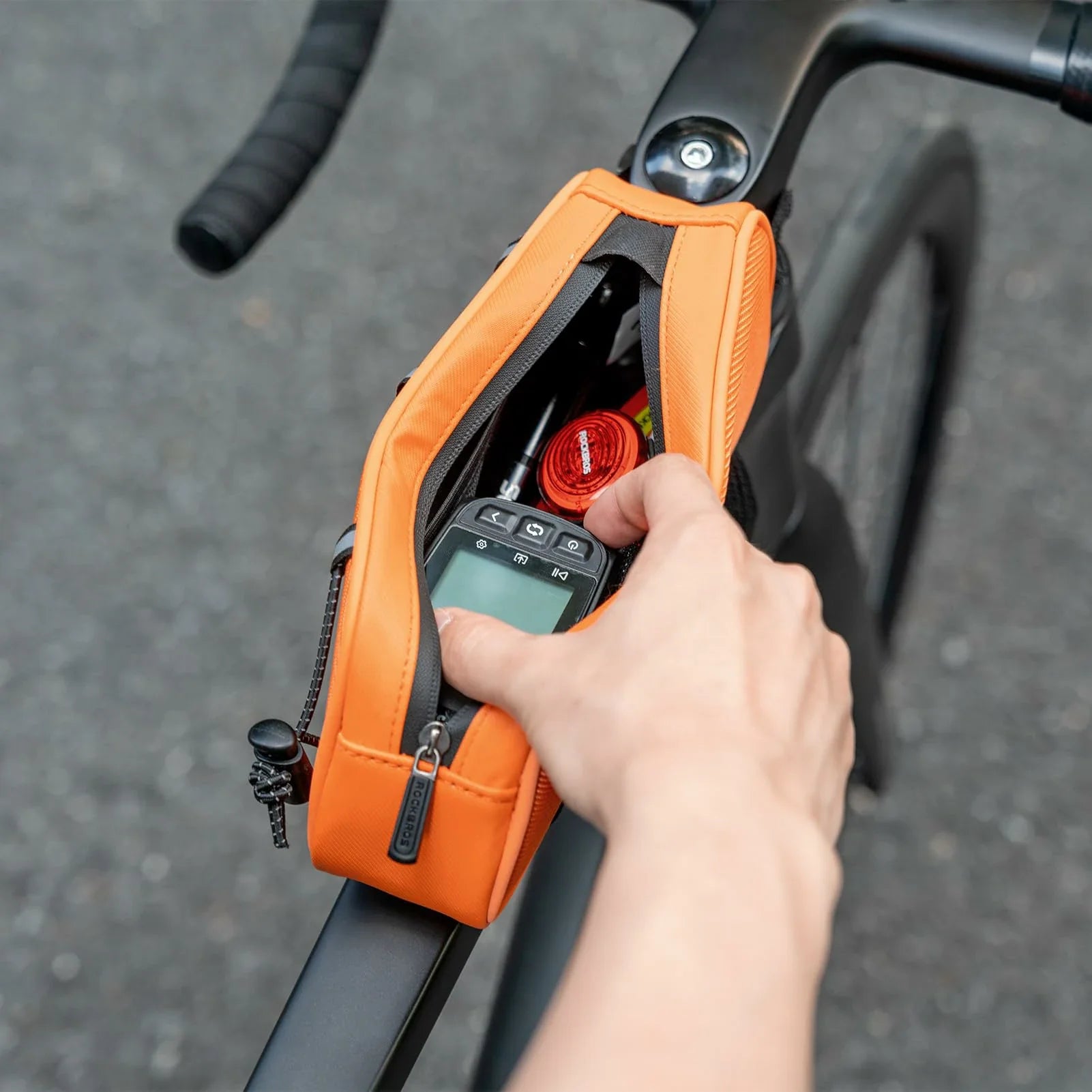 Hand holding an orange device with a screen on a bicycle frame #color_orange