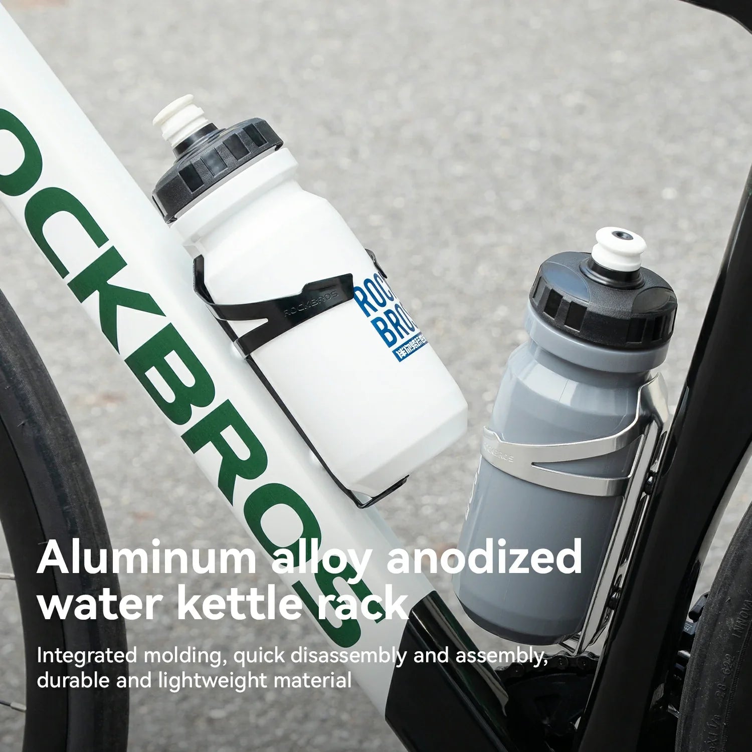 Close-up of a bicycle frame with two RockBros water bottles mounted in black and silver aluminum anodized water kettle racks. White and gray bottles are shown against a blurred gray pavement background, with descriptive text overlaid at the bottom.
