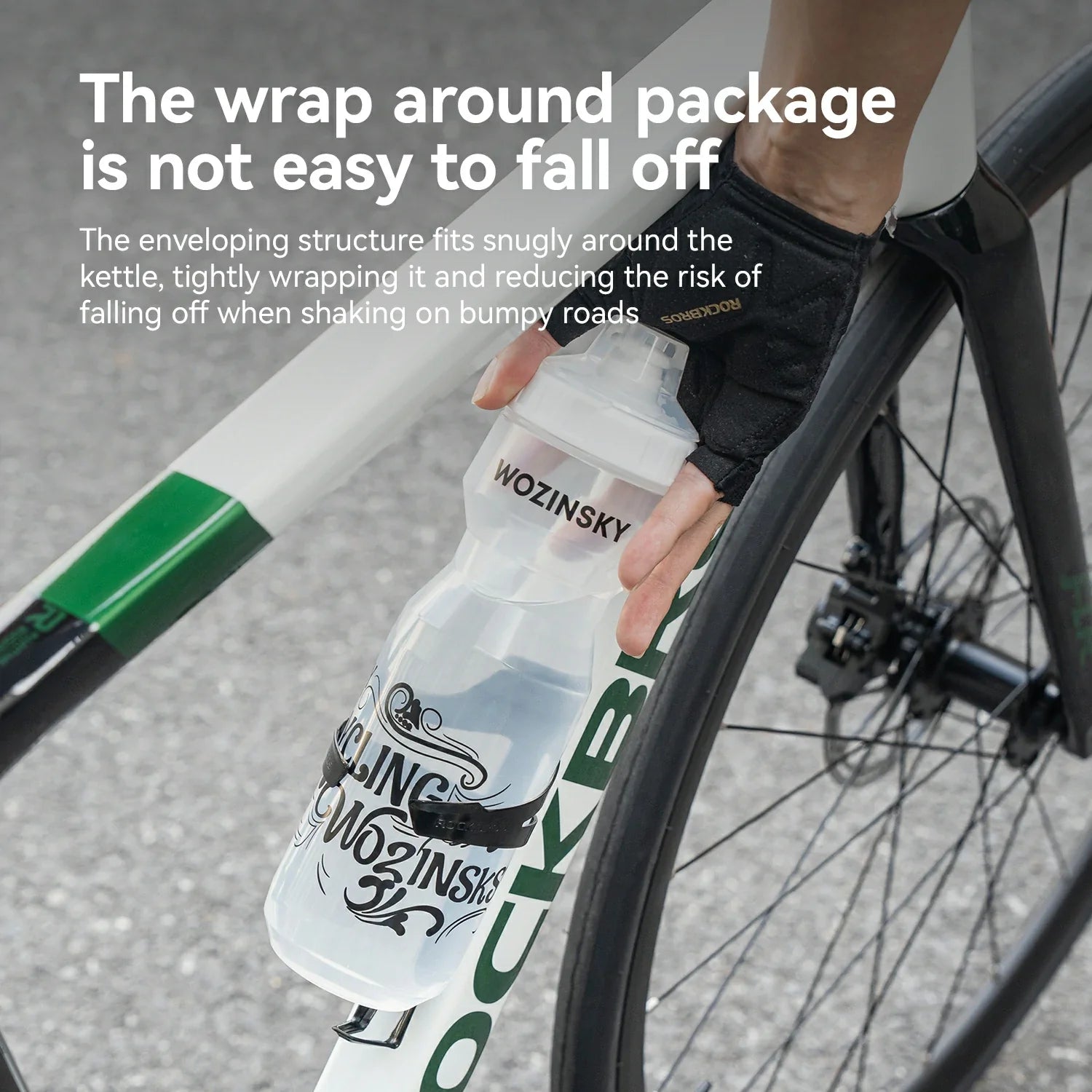 A close-up of a person's hand wearing a black cycling glove and holding a clear Wozinsky cycling bottle with a black and white label, wrapped around a road bike frame and wheel. White text at the top explains the bottle's secure wrap design.