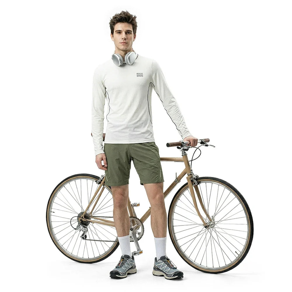 Man standing next to a bicycle wearing a white long-sleeve shirt and green shorts on a white background