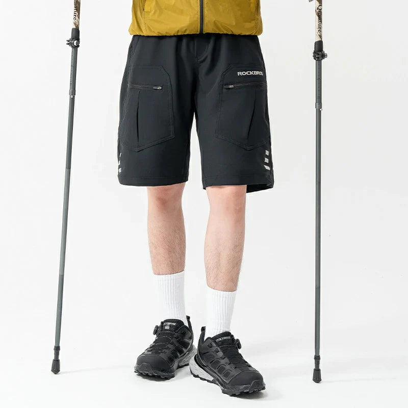 Person wearing black hiking shorts with 'ROCKBROS' branding, standing between two hiking poles on a white background.