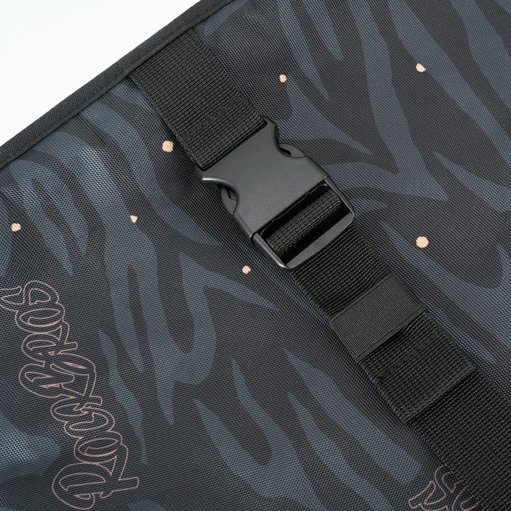 Close-up of a black strap with a buckle on a dark camouflage-patterned surface.