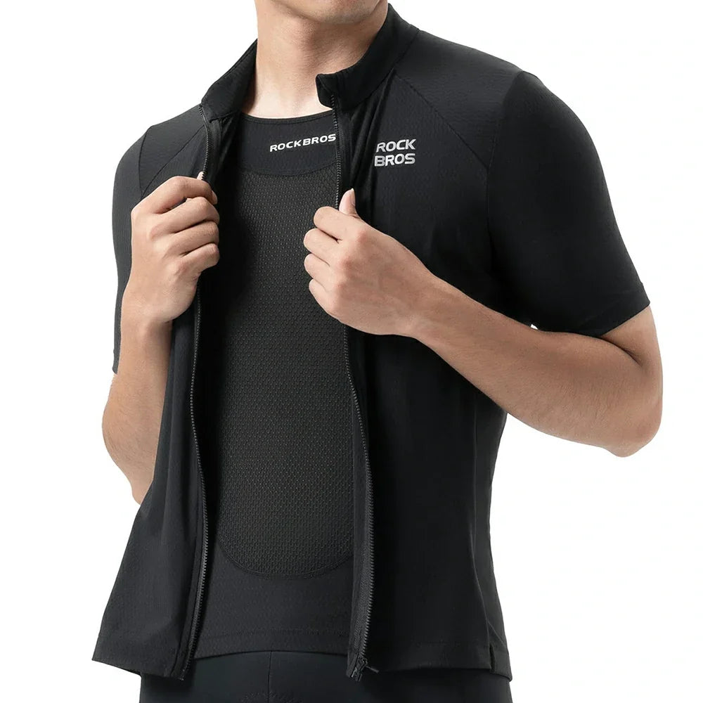 A close-up of a person wearing a black short-sleeve cycling jersey vest over a black cycling jersey. The vest has a high collar, front zipper, and white ROCK BROS branding on the chest, with the brand also visible on the inside neck label. #Color_Black