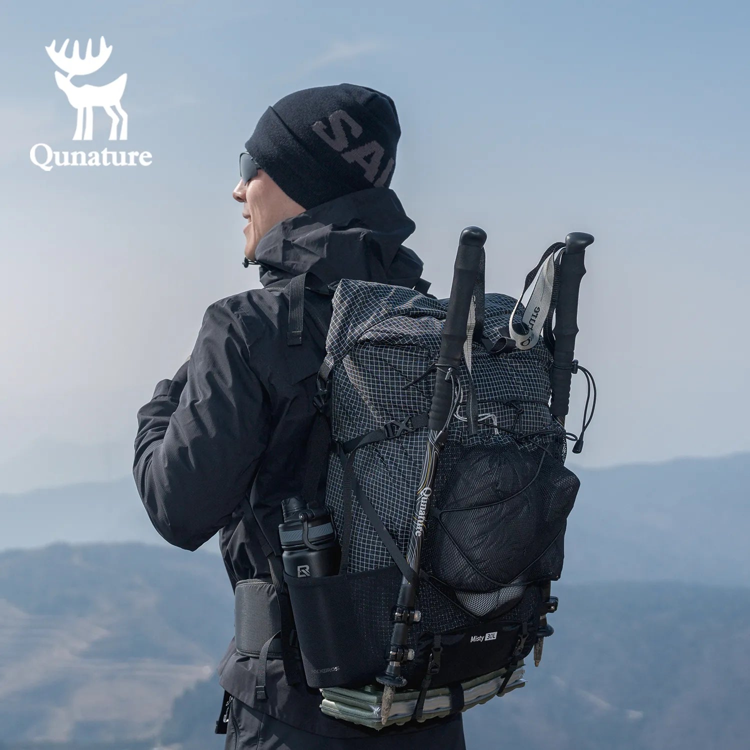 A man wearing a hat and sunglasses and carrying a black backpack is looking into the distance on the mountain