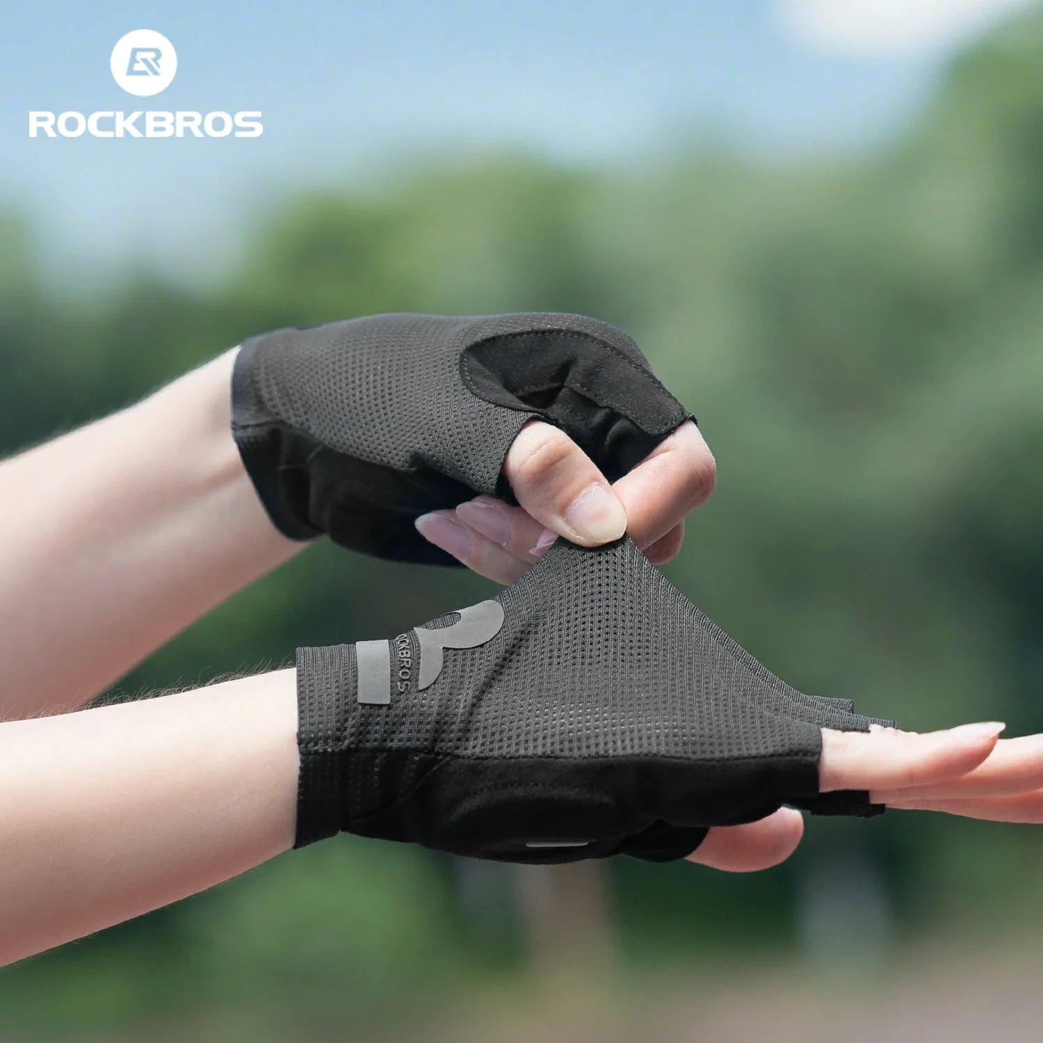 Black gloves being held with a blurred green background and 'RockBros' logo.  #color_black