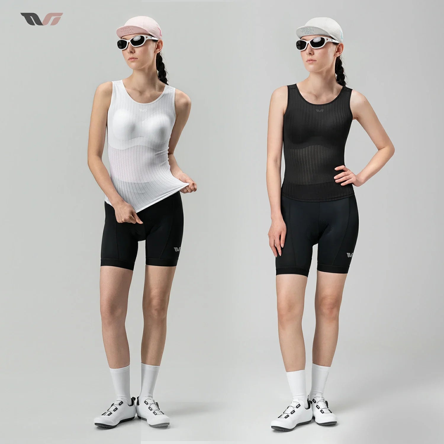 Two female models standing side by side in a studio, each wearing a sleeveless athletic compression top and matching fitted shorts. The left model wears a white top with black shorts, a pink cap, sunglasses, white socks, and white shoes.