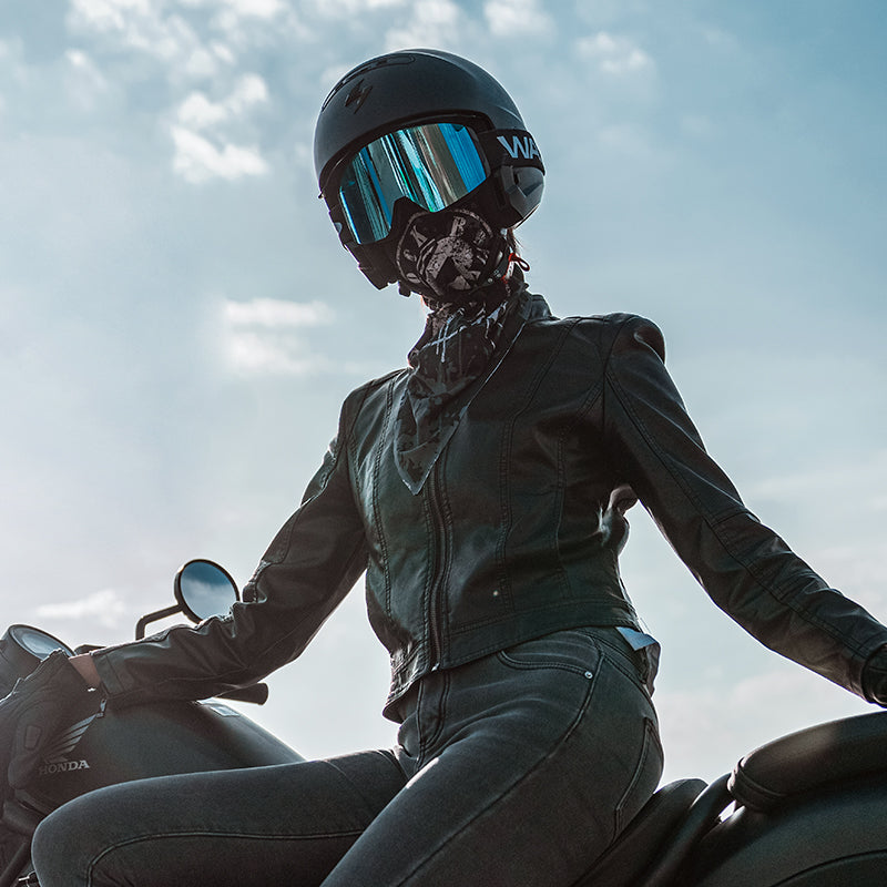 Person wearing a black helmet and leather jacket sitting on a motorcycle against a cloudy sky.